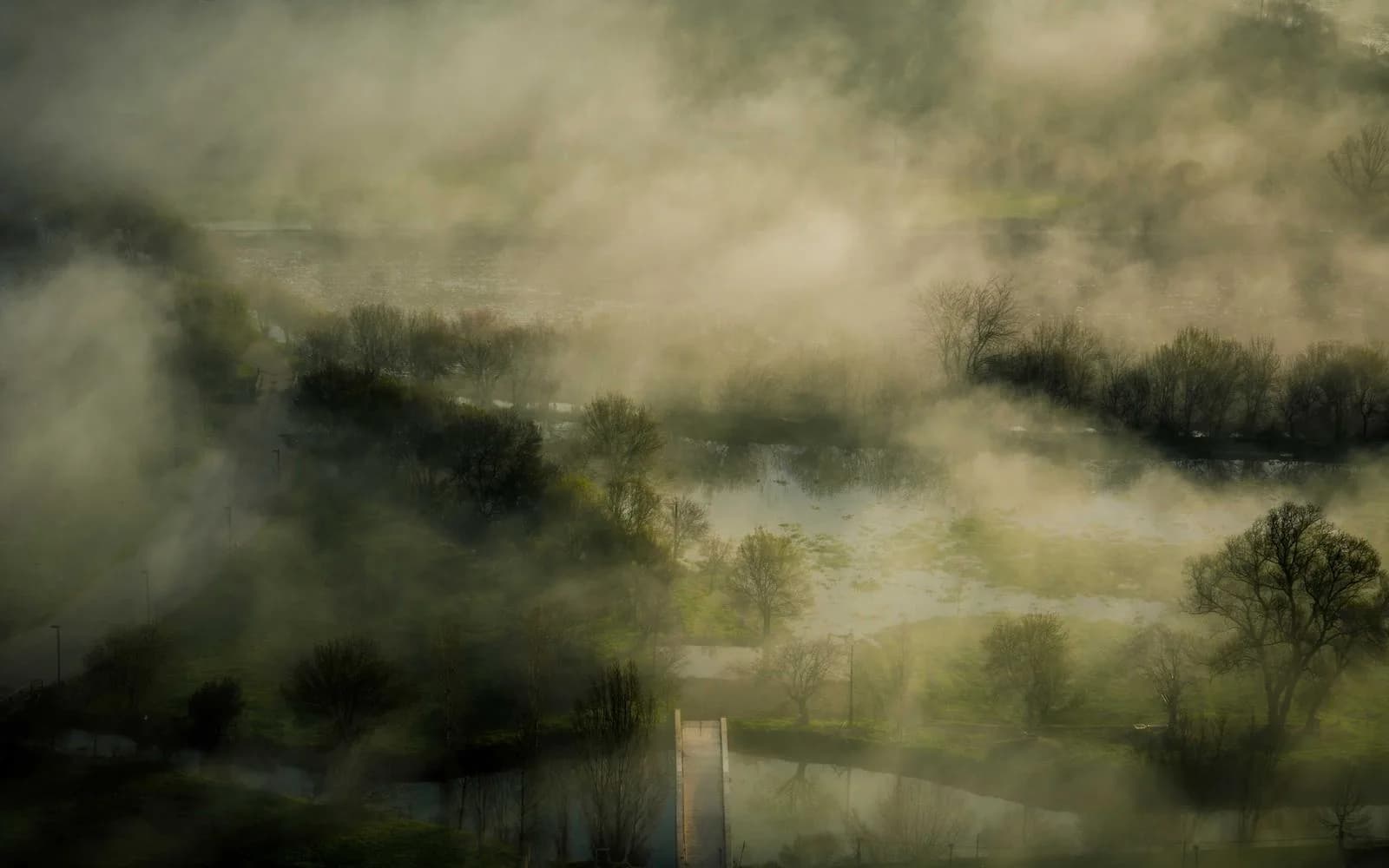 An aerial view of a misty river winding through green fields