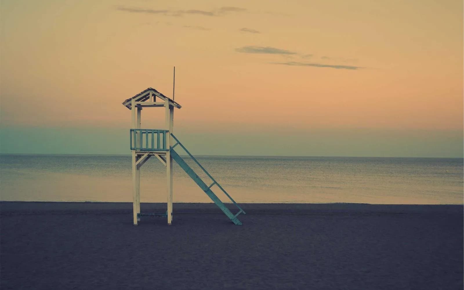 A weathered wooden lifeguard tower on an empty beach at dusk