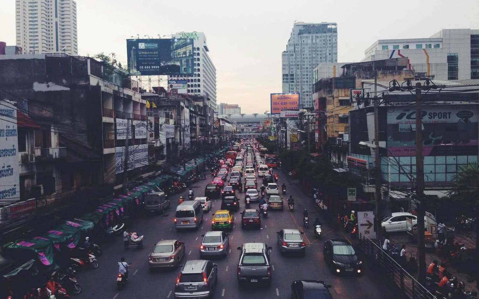 A busy city street jammed with cars, motorbikes and market stalls