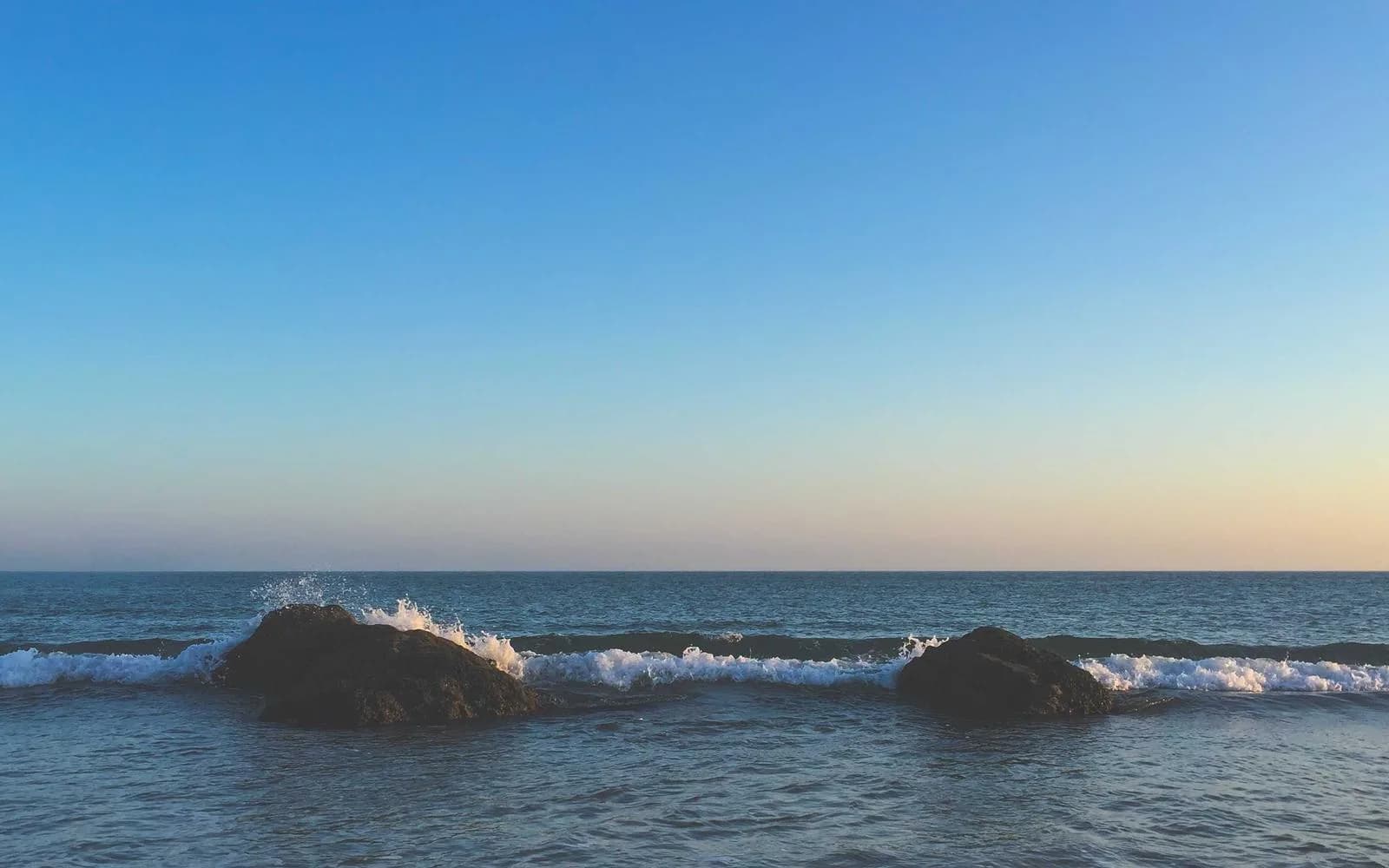 Waves breaking over dark rocks on a coastline at dusk