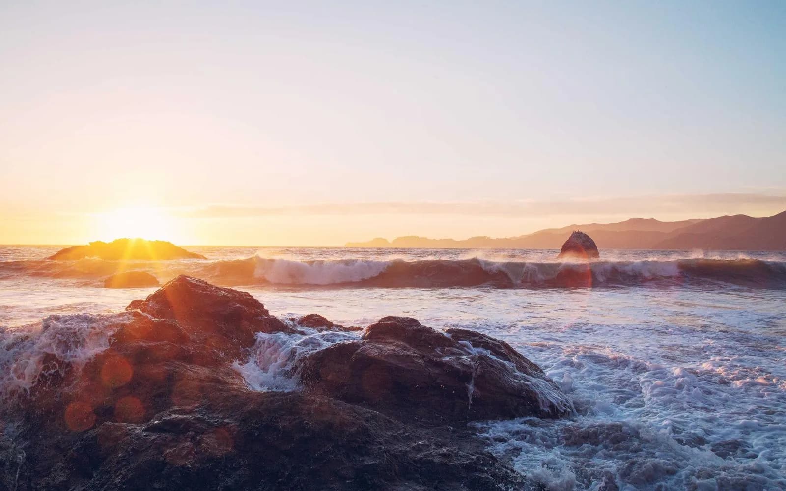 The sun rising over a rocky coastline with breaking waves
