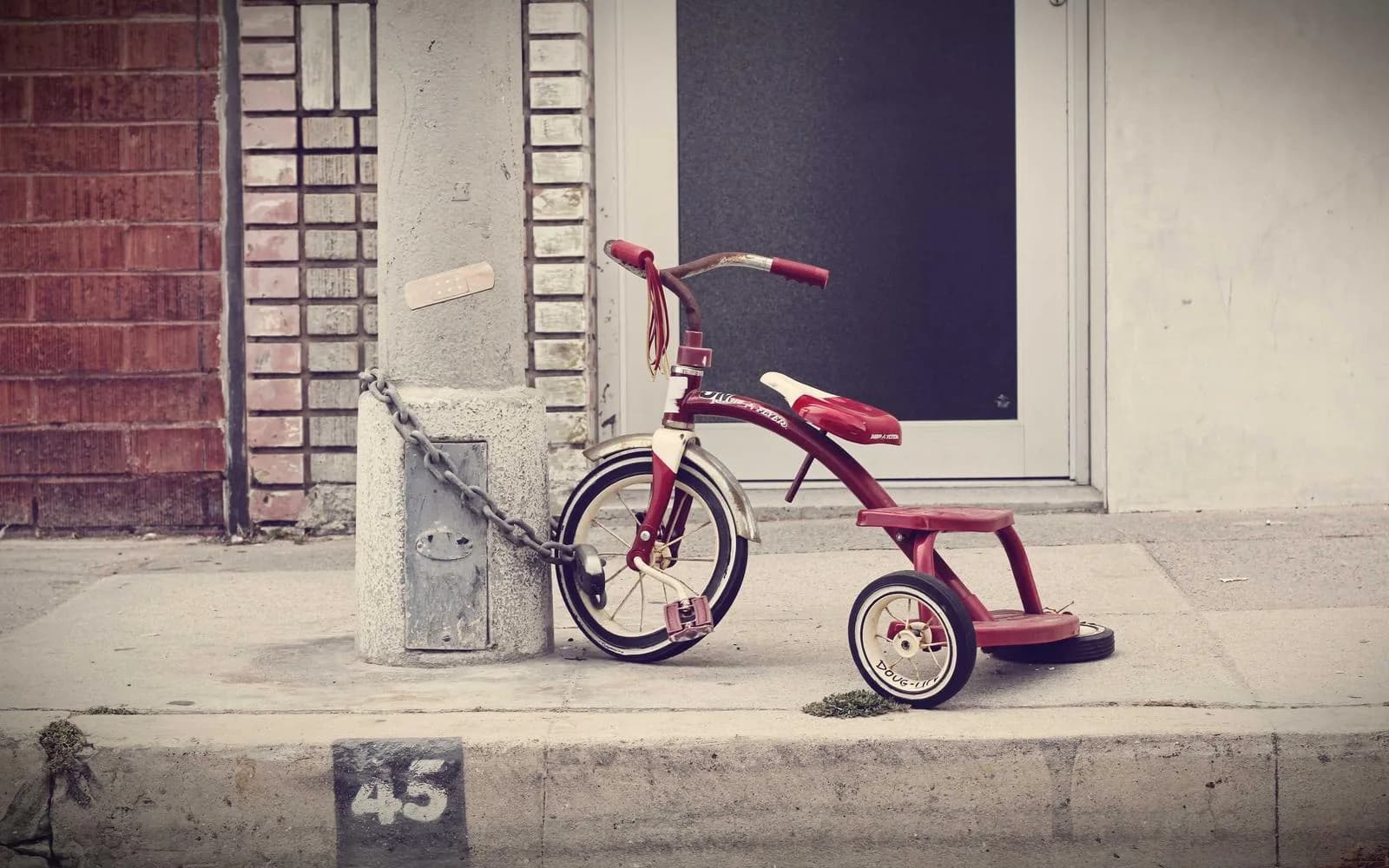 A child's tricycle chained to a post on a city sidewalk