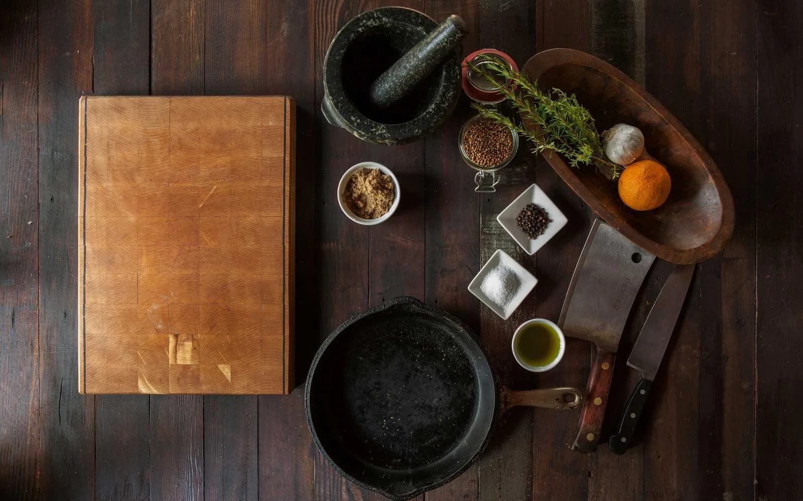 Overhead view of a rustic kitchen counter with knives, spices and a cast-iron pan