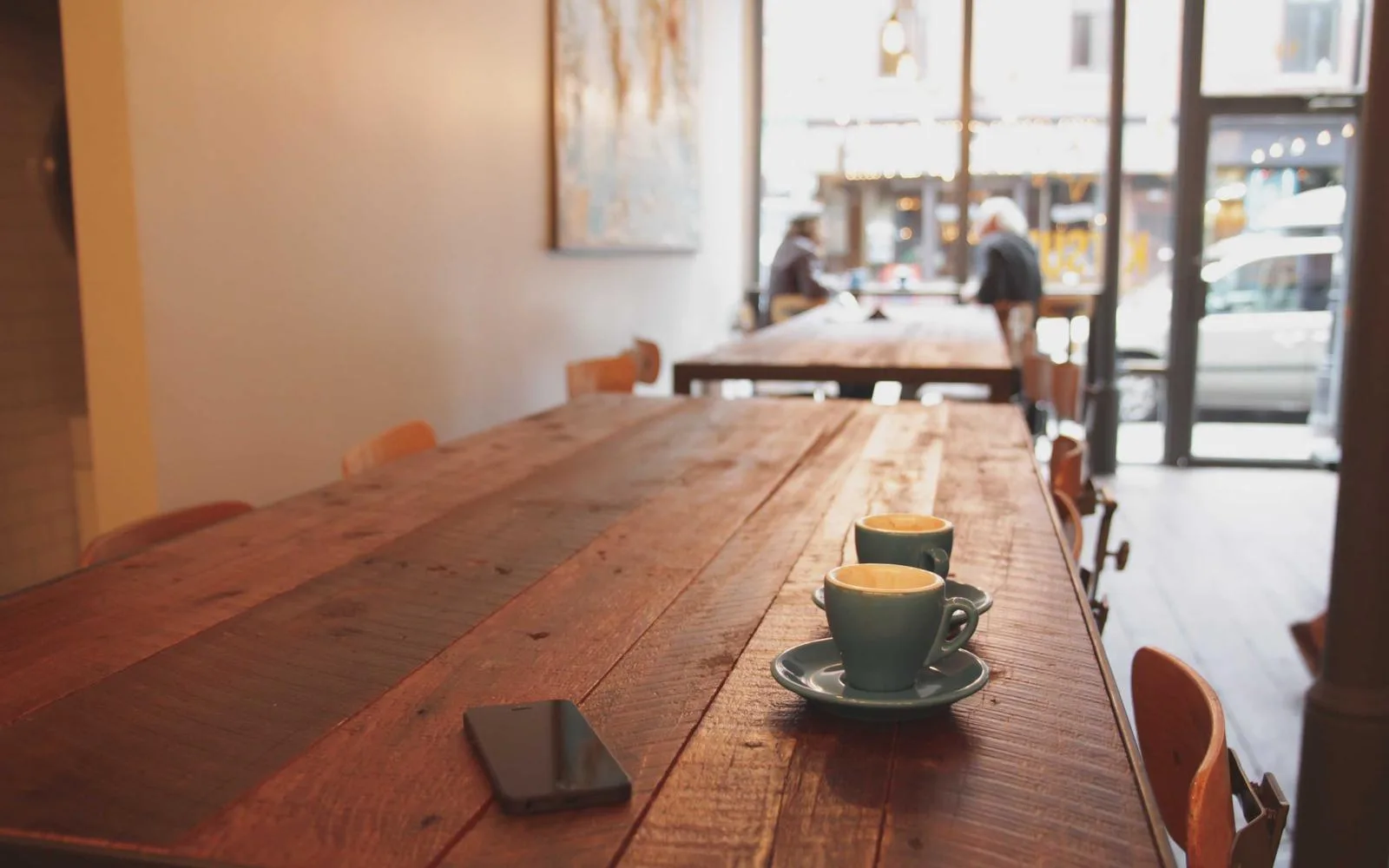 Two espresso cups and a phone on a wooden café table