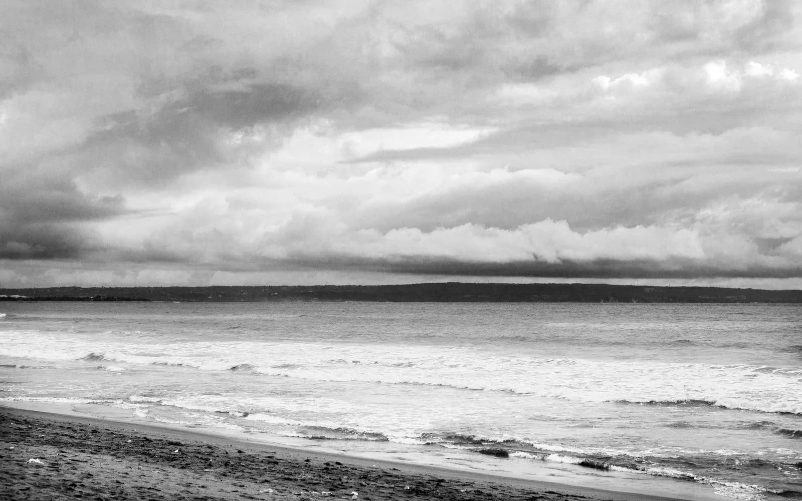A black-and-white photo of waves rolling onto a beach under stormy skies