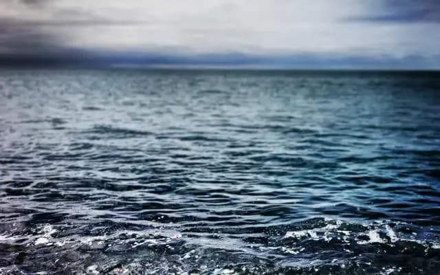 A calm, dark blue sea under an overcast sky