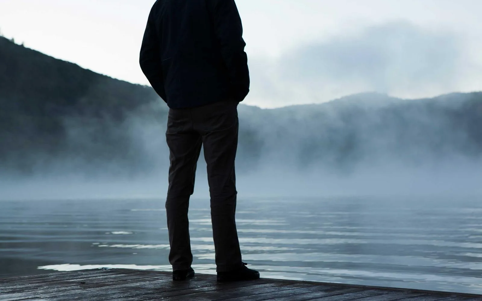 A person standing on a dock looking out over a misty lake